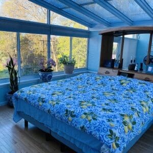 A bed with blue sheets and pillows in front of a window.