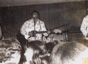 A man playing guitar in front of a crowd.