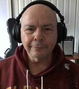 A bald man wearing headphones and looking at the camera.