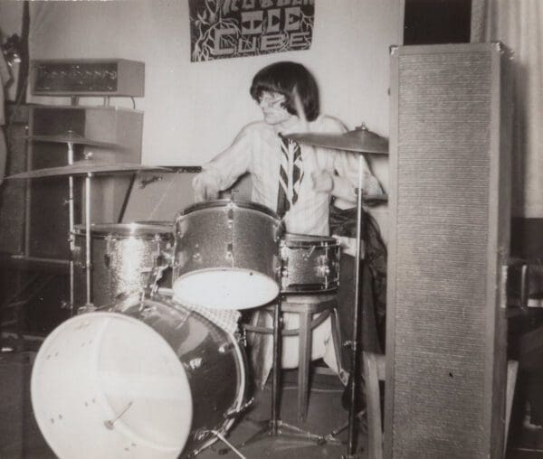 A young man playing drums in his room.