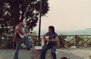 Two men playing guitar and singing on a hill