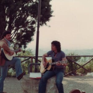 Two men playing guitar and singing on a wall.